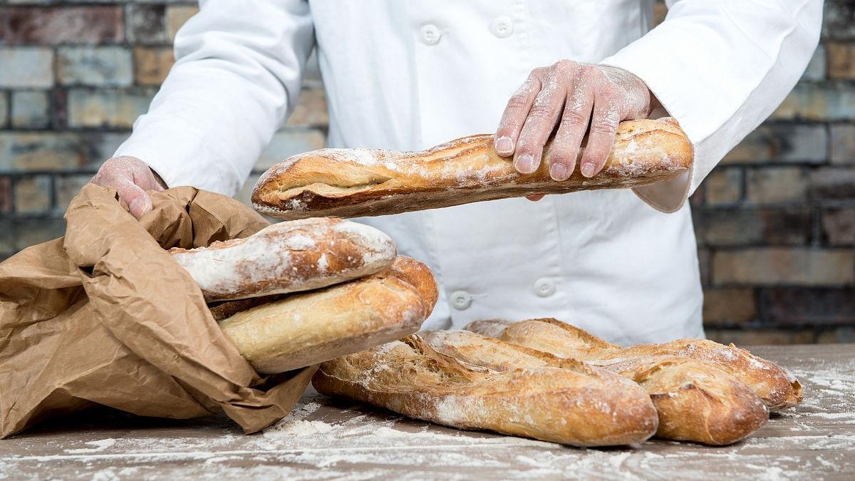 village baker in rural Europe, hand-kneading dough, wooden bakery, traditional oven, old man in apron, authentic local scene